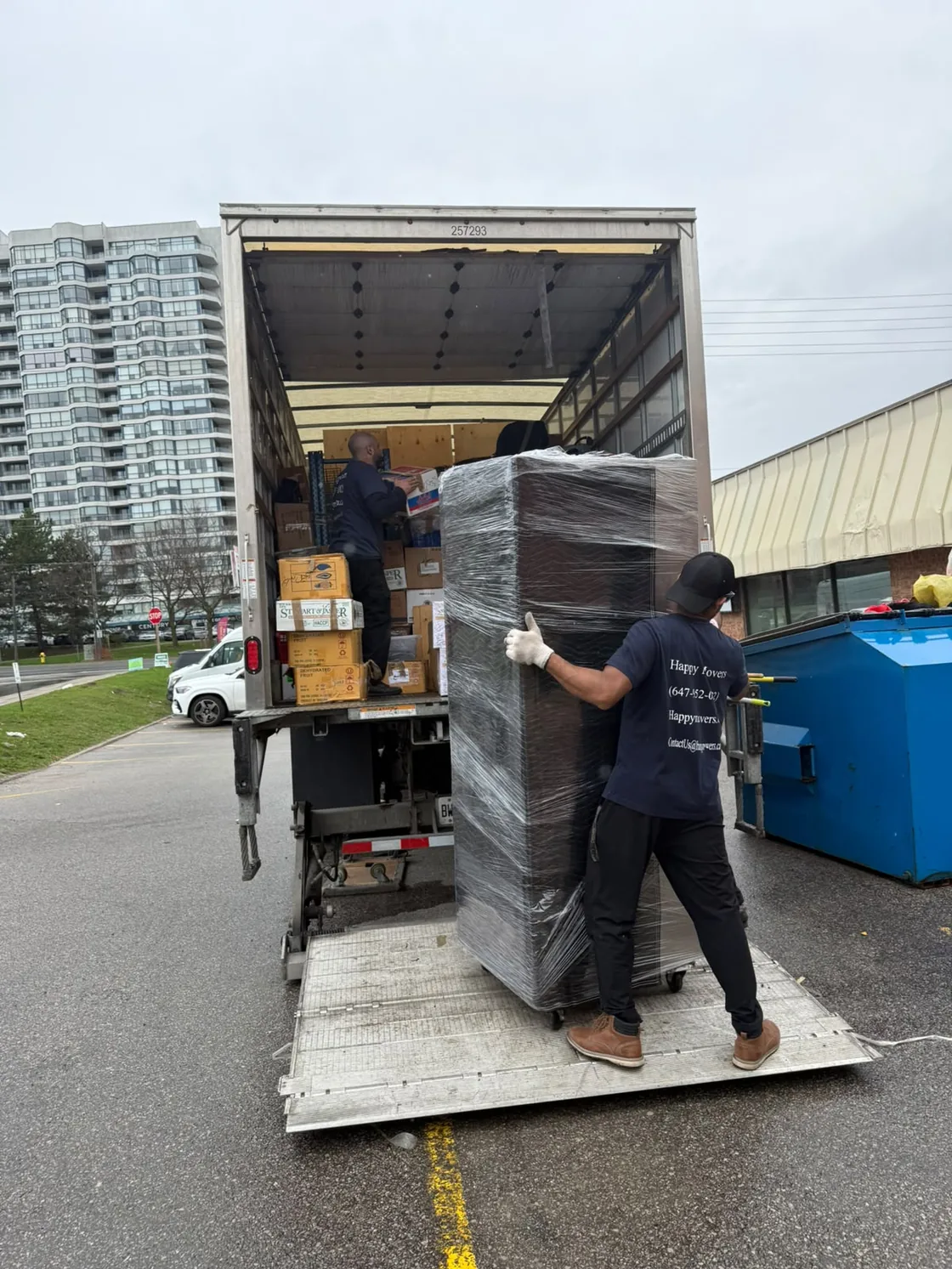 Happy Movers crew wheeling a wrapped item toward a Toronto high-rise building