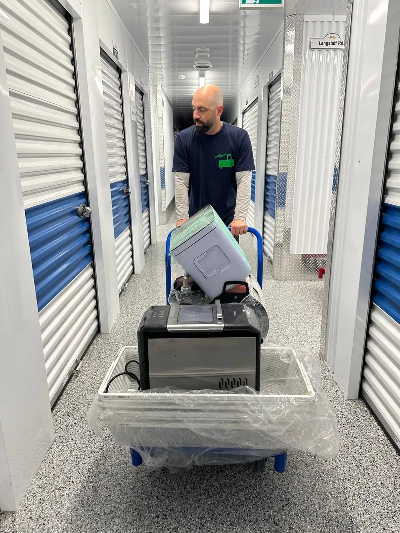 Mover wheeling a loaded dolly through a storage facility corridor